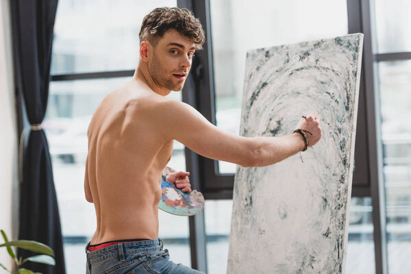 handsome half-naked artist looking at camera while painting picture