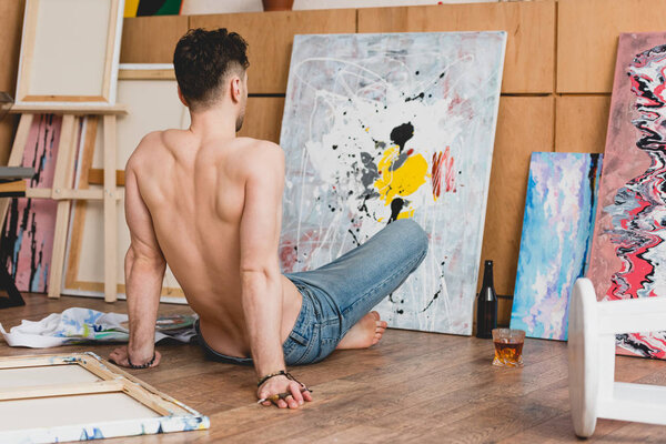 back view of half-naked artist sitting on floor and looking at painted picture