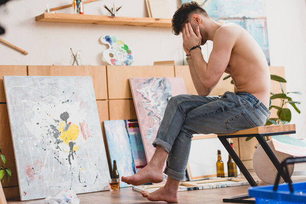 exhausted artist sitting on chair in painting studio and holding hands on head