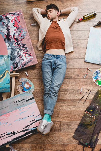 overhead view of tired artist sleeping on floor in painting studio