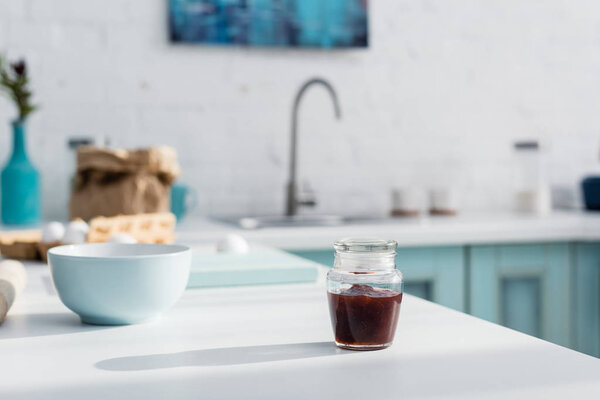 glass jar with tasty red jam near bowl on kitchen table