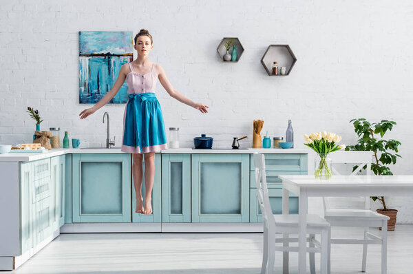 beautiful barefoot girl in apron levitating in air in kitchen