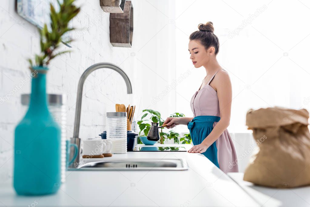 selective focus of elegant girl preparing coffee in cezve in kitchen 