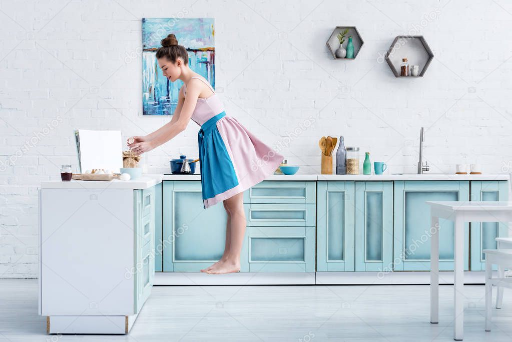 young barefoot woman levitating in air while cooking in kitchen