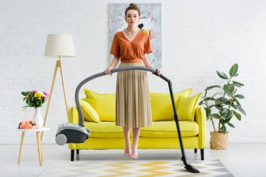 havada levitating ve elektrikli süpürge tutan zarif yalınayak genç kadın