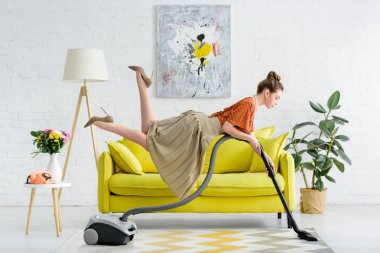 havada levitating ve oturma odasında halı vakumlama zarif konsantre genç kadın yan görünüm