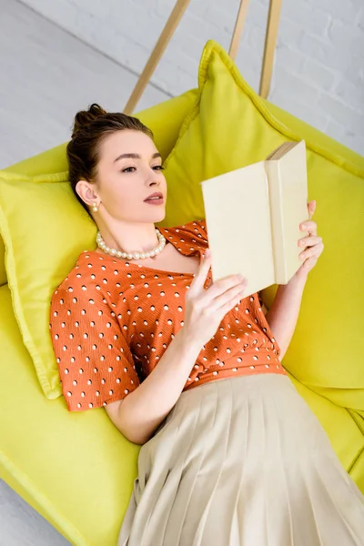 黄色のソファーで本を読みながら休憩魅力的なエレガントな若い女性 — ストック写真