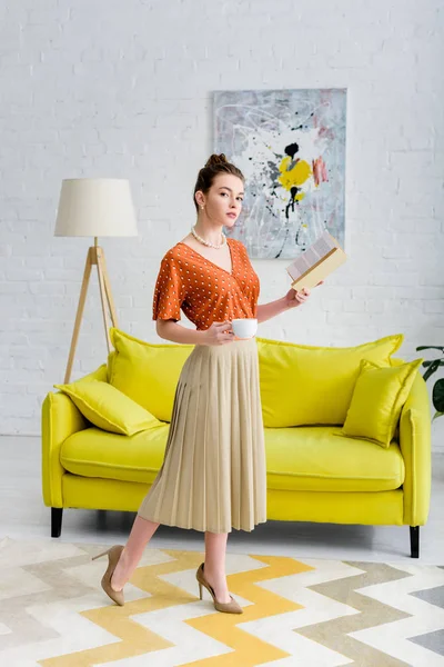 Elegant Young Woman Holding Book Coffee Cup Living Room — Stock Photo, Image
