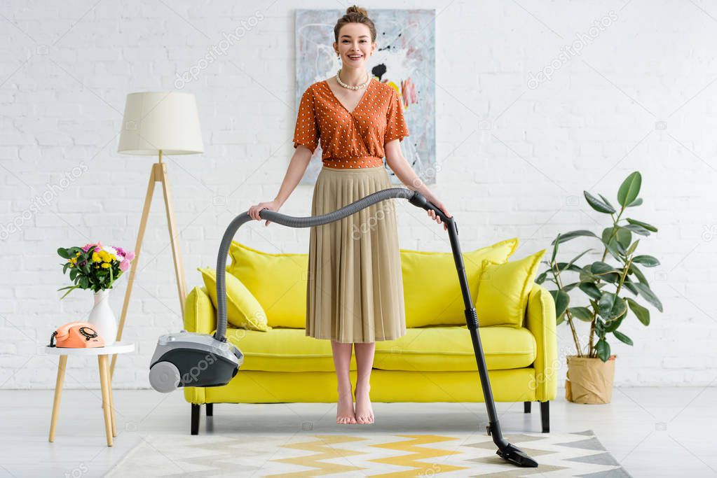 elegant smiling barefoot young woman levitating in air and holding vacuum cleaner
