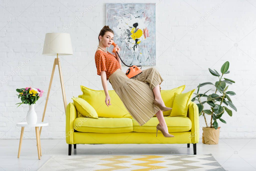 elegant young woman levitating in air and talking on vintage phone in living room