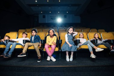 sinema oturan ve film izlerken çok kültürlü arkadaşlar gülümseyen