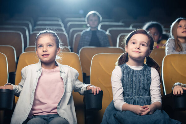 smiling children watching movie in cinema together with multicultural friends