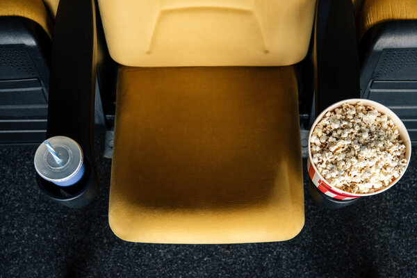 top view of orange cinema seat with paper cups of soda and popcorn in cup holders