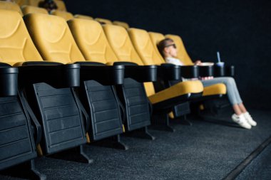 selective focus of child sitting in cinema seat in empty row clipart