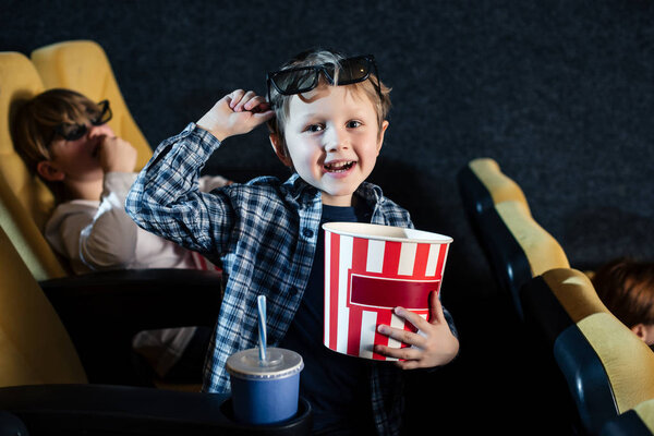 избирательный фокус улыбающегося мальчика, держащего бумажную чашку попкорна и смотрящего в камеру
