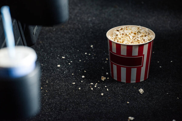 selective focus of stripped red and white paper cup with popcorn on floor