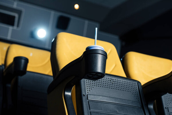 selective focus of cinema seat with disposable cup with straw in cup holder