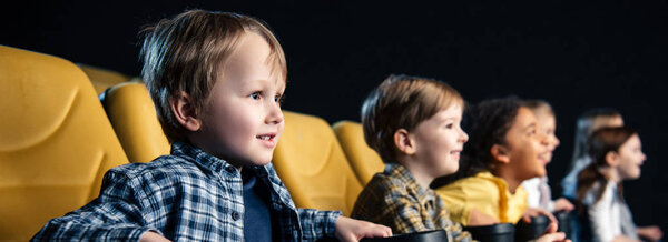 panoramic shot of smiling multicultural friends watching movie in cinema together