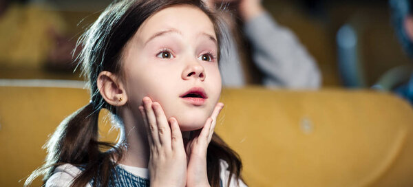 панорамный снимок эмоционального ребенка, смотрящего кино и держащегося за руки возле лица
