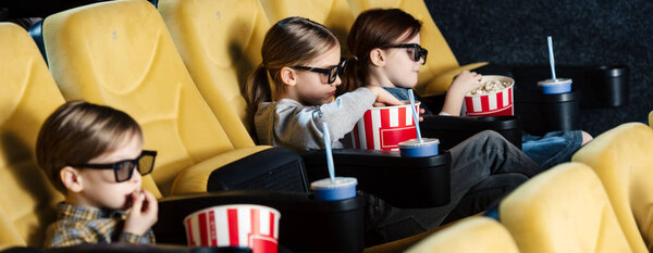 panoramic shot of children watching movie in 3d glasses and eating popcorn in cinema