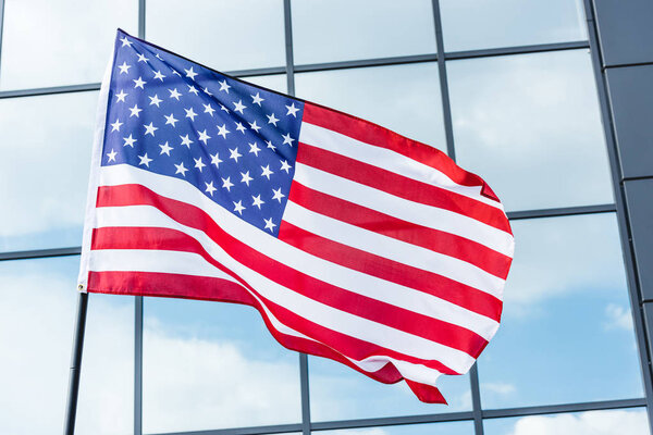 stars and stripes on flag of america near building with glass windows and sky reflection