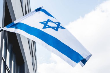 low angle view of national israel flag with star of david near building against blue sky clipart