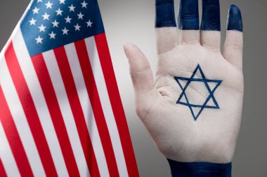 selective focus of female hand with jewish star of david near american flag on grey  clipart