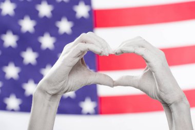 cropped view of female hands painted in white showing heard-shaped sign near american flag clipart