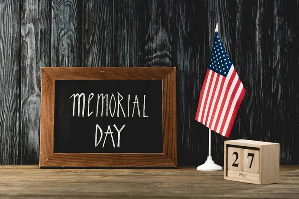 chalkboard with memorial day lettering near american flag and wooden cubes with date