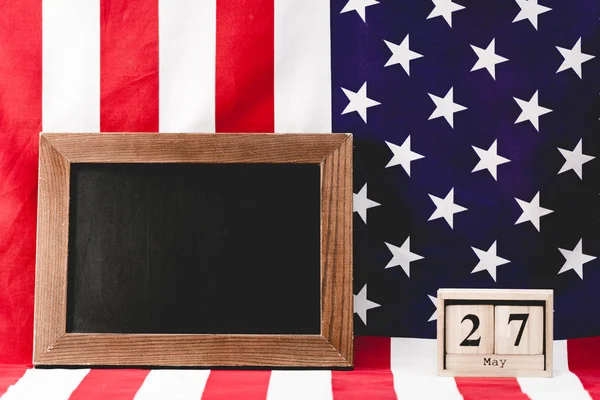 empty black board near american flag and wooden cubes with date 