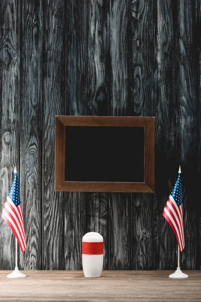 empty black board near funeral urn with ashes and american flags