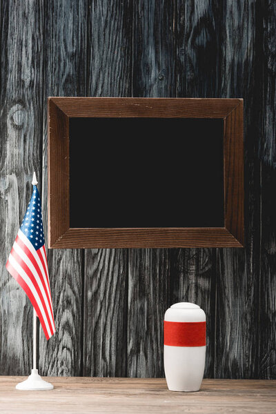empty chalkboard near funeral urn with ashes and american flag