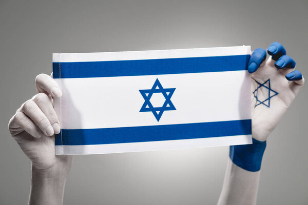 cropped view of female hands holding national flag of israel on grey