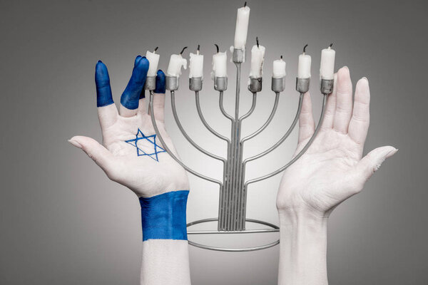 обрезанный вид женских рук со звездой Давида возле подсвечника на сером
