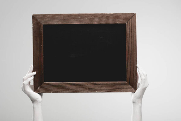 cropped view of female hands painted in white holding empty chalkboard isolated on grey 