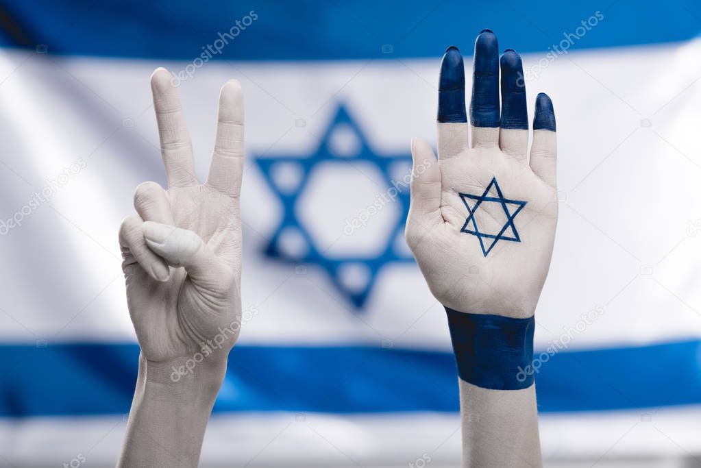 cropped view of female hands with star of david showing peace sign near flag