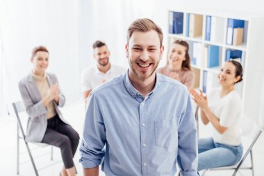 gülümseyen adam grup terapi seansı sırasında oturan insanlar ise kamera bakıyor