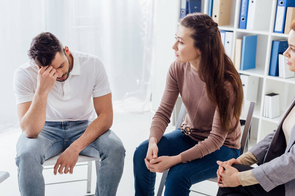 women and upset man sitting on chairs during group therapy session