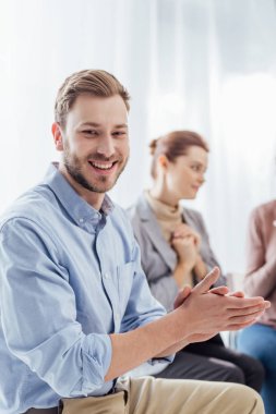gülümseyen seçici odak adam kameraya bakarak ve grup terapi seansı sırasında alkış
