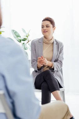 selective focus of woman in formal wear sitting and looking away during therapy session clipart