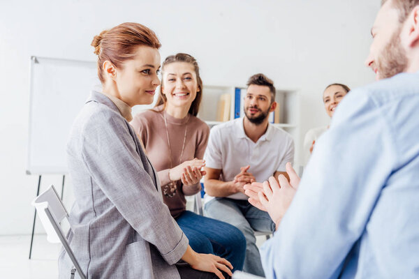 smiling people sitting and applauding during group therapy meeting