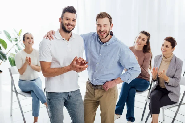 Dois Homens Sorridentes Olhando Para Câmera Enquanto Pessoas Sentadas Aplaudindo — Fotografia de Stock