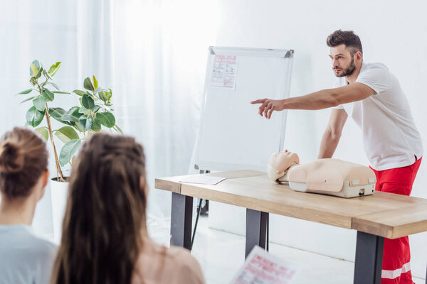 handsome instructor with cpr dummy pointing with finger during first aid training class