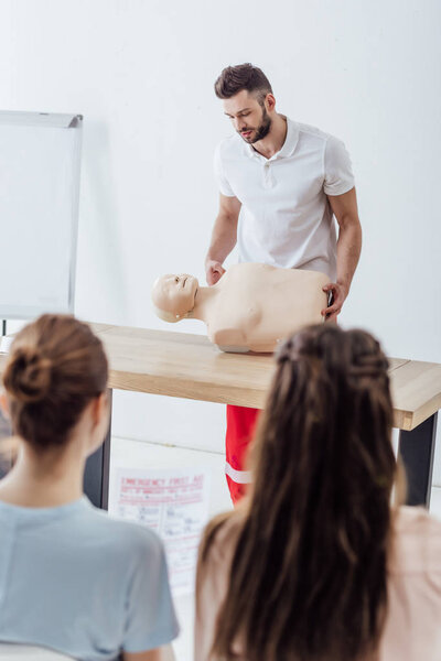 selective focus of handsome instructor with cpr dummy during first aid training class