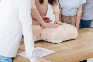 cropped view of group of people during first aid training class with cpr dummy clipart