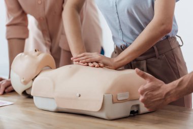 cpr eğitim sınıf sırasında yukarı işareti yapan erkek sırasında kukla üzerinde göğüs sıkıştırma gerçekleştirerek kadın kırpılmış görünümünü