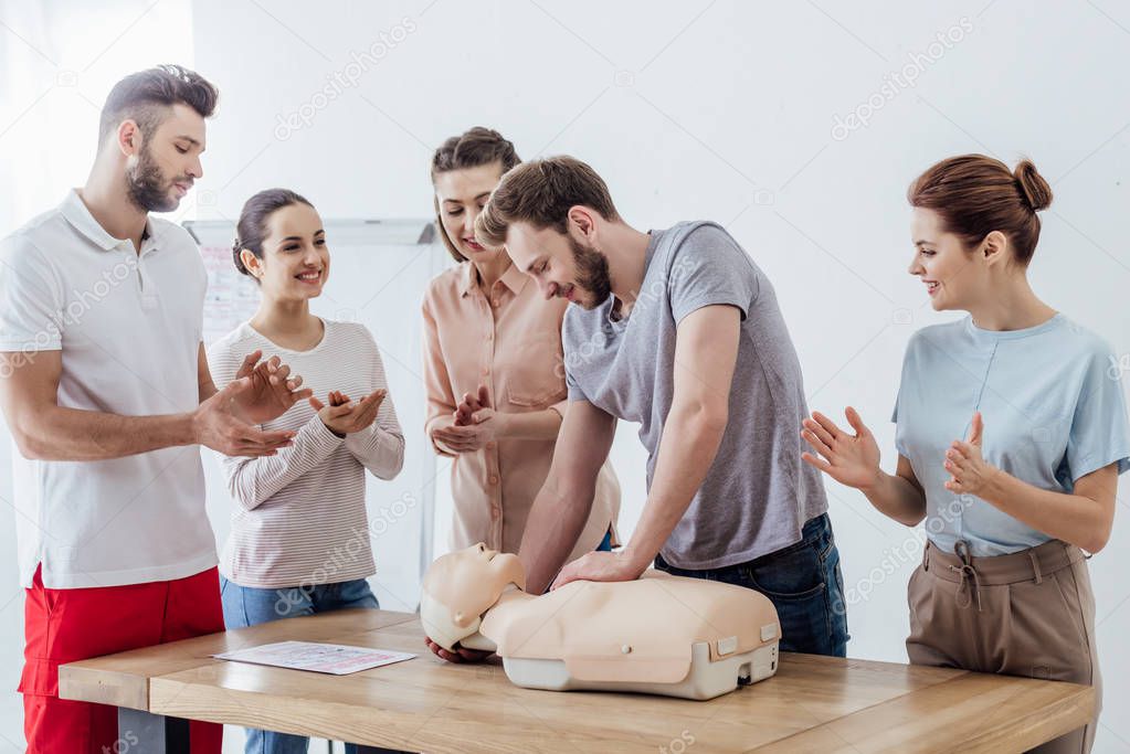group of people applauding while man performing cpr on dummy during first aid training