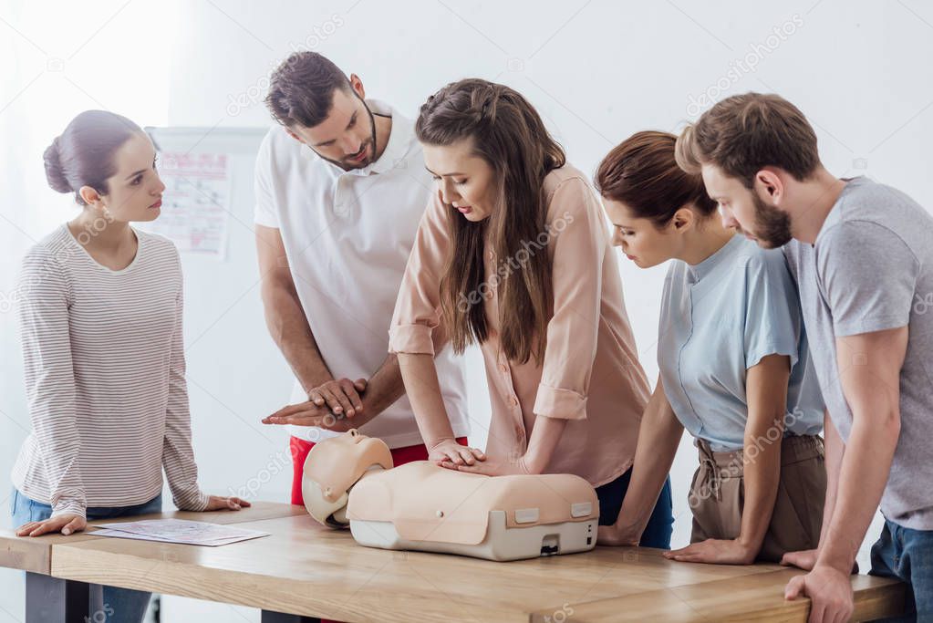 group of concentrated people performing cpr on dummy during first aid training