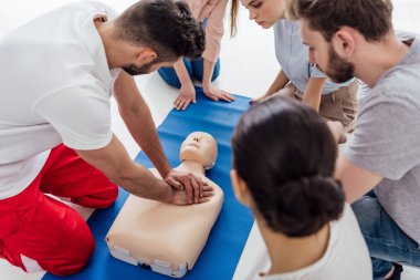 instructor performing cpr on dummy during first aid training with group of people clipart