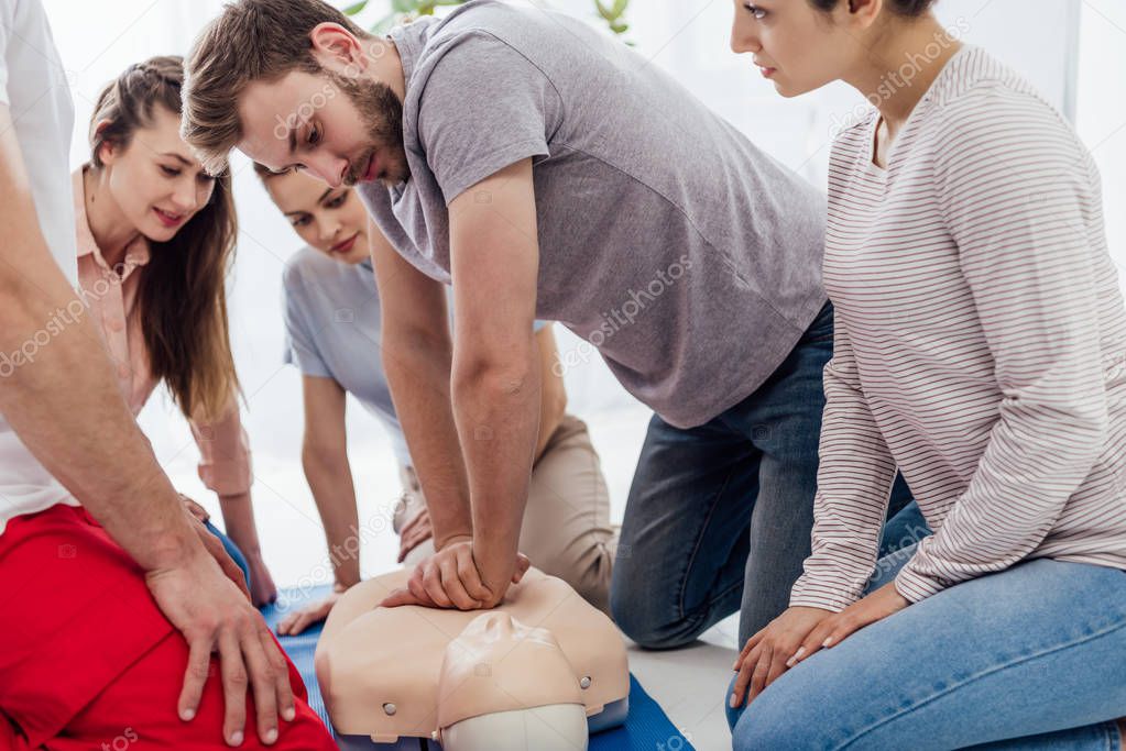 group of people looking at man performing cpr on dummy during first aid training